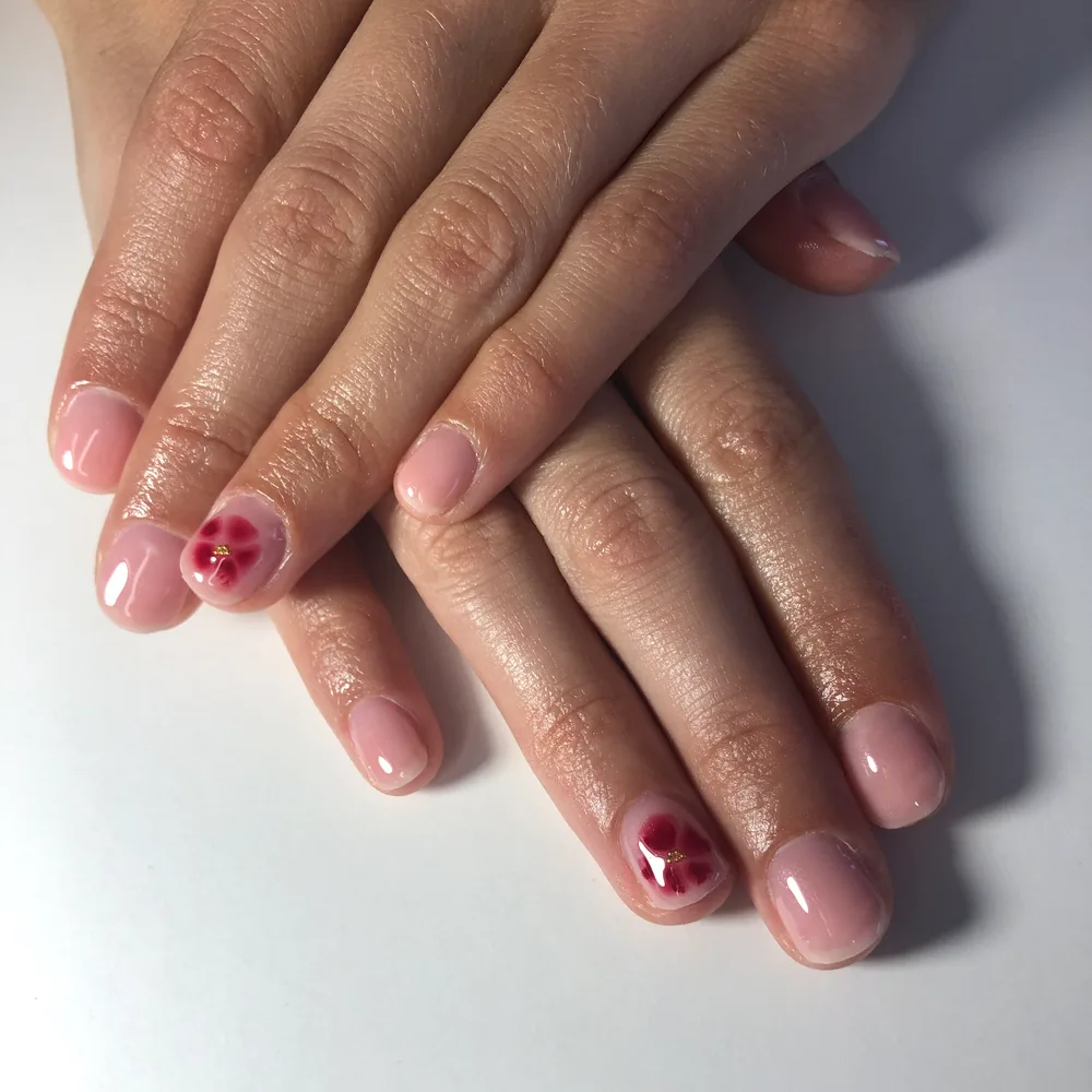 Semi-permanent nude rosé sur ongles naturels très courts, une fleur rouge peinte sur l'annulaire
