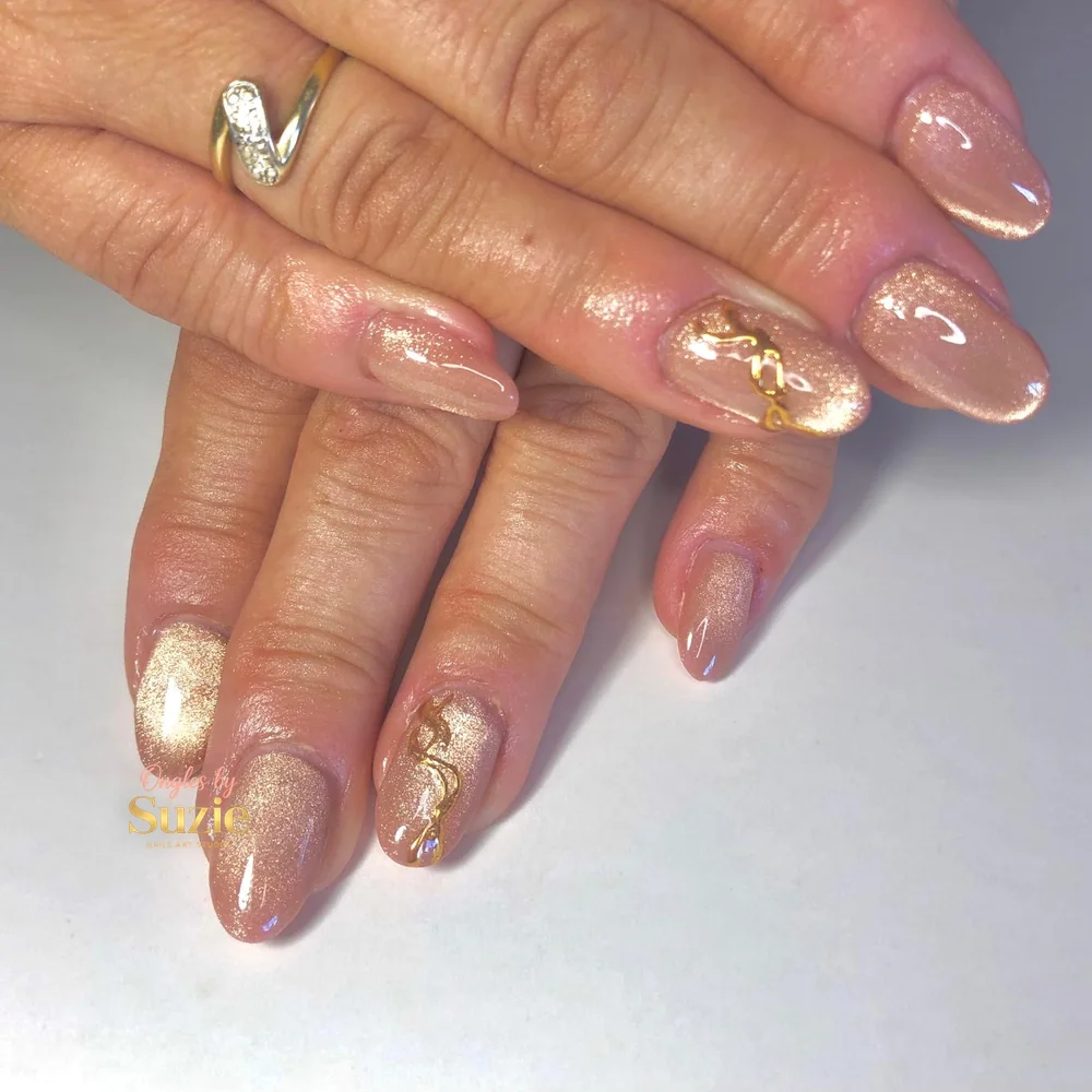 Ongles amande nude à effet œil-de-chat doré, bijoux d'ongle dorés posés sur l'annulaire de chaque main