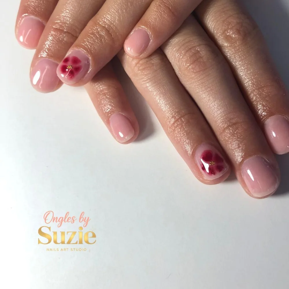 Semi-permanent nude rosé sur ongles naturels courts, une fleur rouge au cœur doré peinte sur l'annulaire